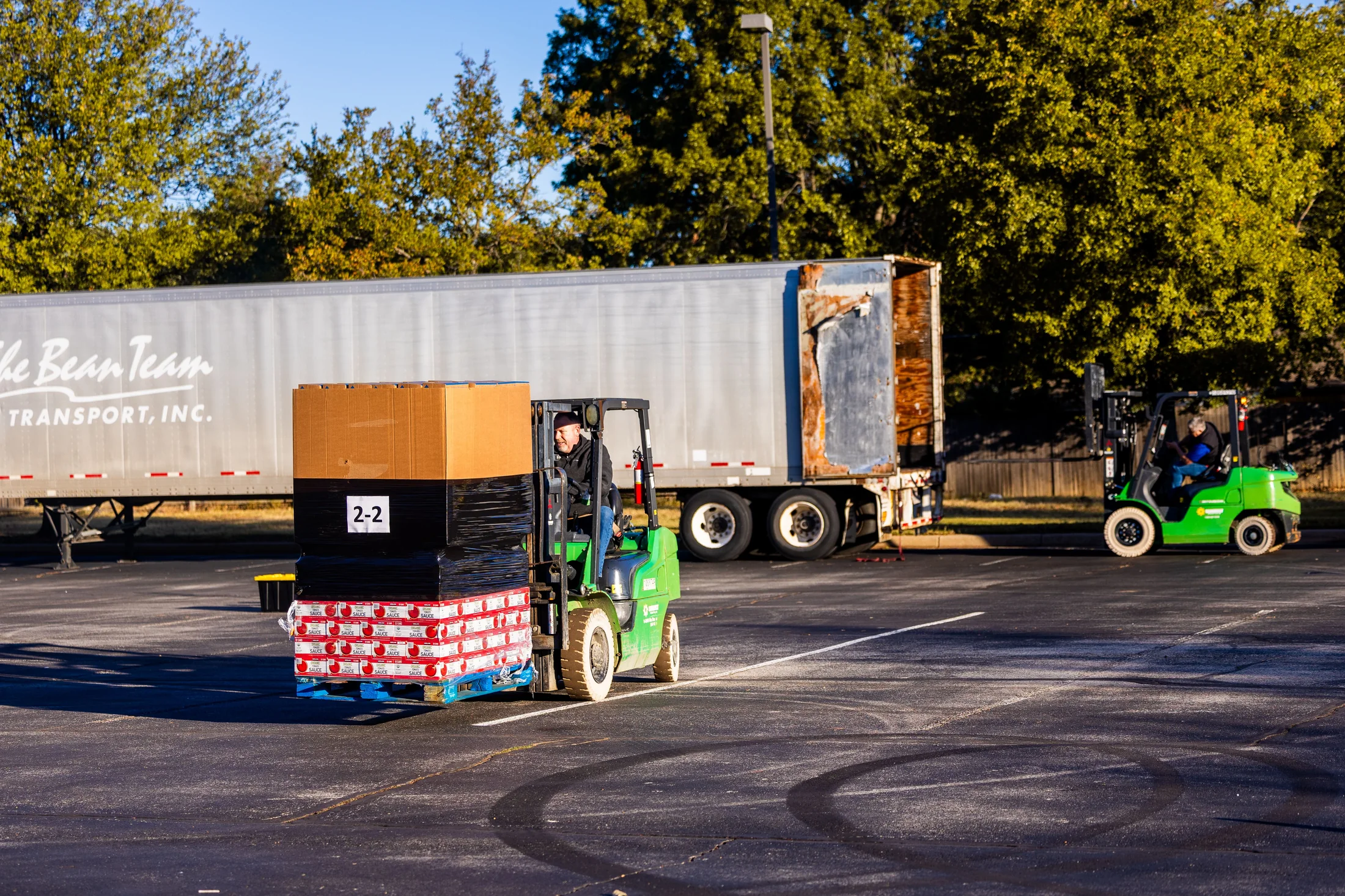 Forklift operators moving palletized cargo beside a semi-trailer